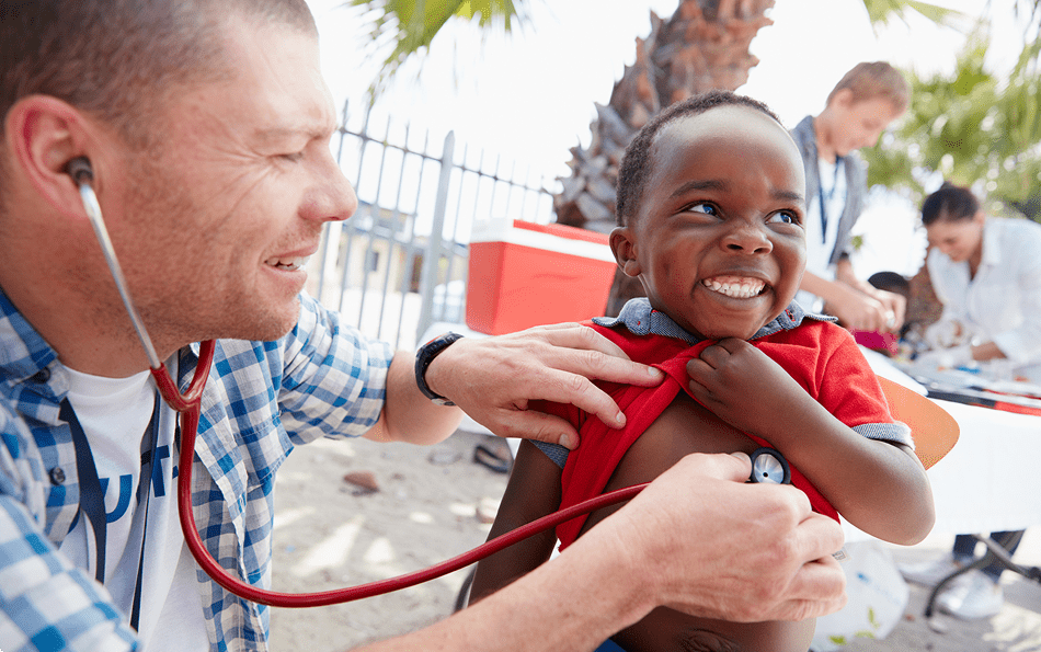 Doctor examining smiling child with stethoscope outdoors.